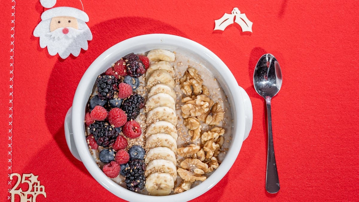 Festive breakfast bowl with blackberries, raspberries, banana, and walnuts on a Christmas tablecloth.